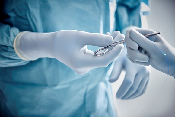Hand mit Handschuhen mit chirurgischem Instrument